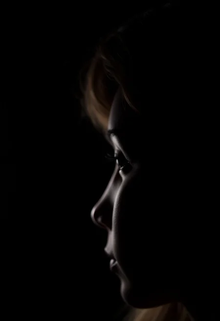 A realistic side profile of a girl against a black background, captured in low lighting, highlighting her face in a simple, moody portrait.
