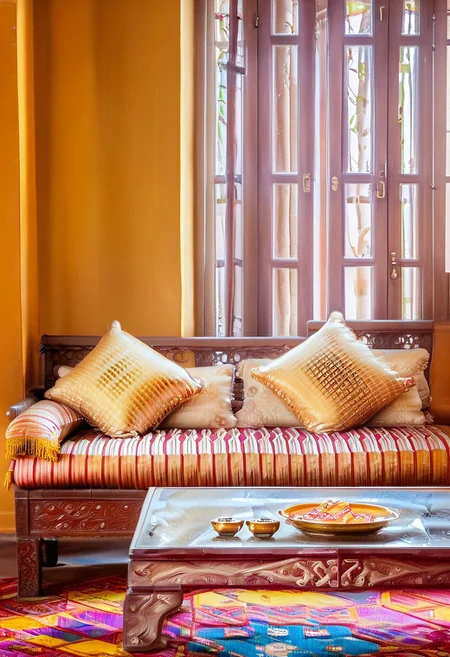 Indian_Interior_SDXL, InteriorType:LivingRoom, A stunning and vibrant modern living room, featuring a traditional Indian sofa. In the center, a golden tray holds small sweets on top of a table, surrounded by a beautiful, intricate pattern. The bokeh background creates a dreamy atmosphere, with soft, blurred lights that accentuate the warm, inviting ambiance of the space.