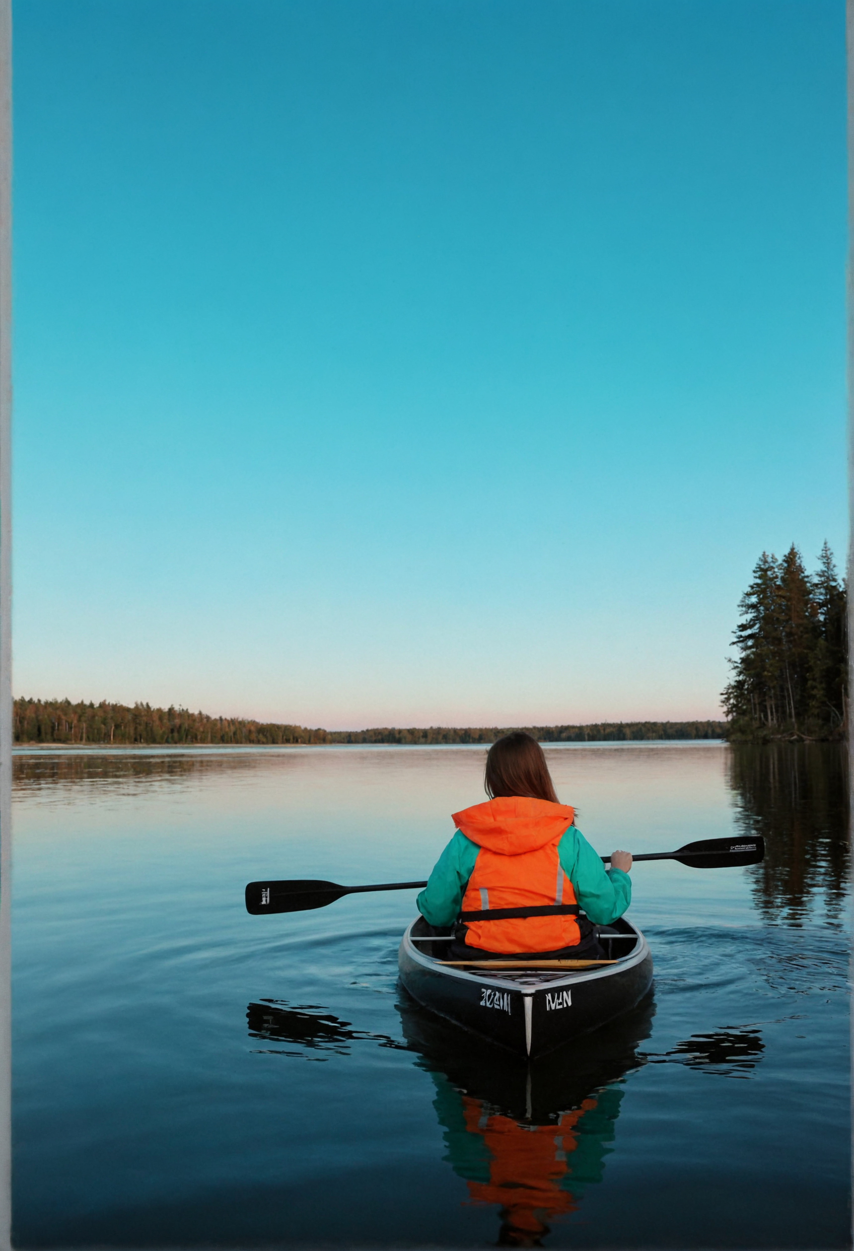 A young woman with long, straight brown hair sits at the front of a small, sleek black canoe, facing away from the camera. She wears a green jacket and an orange life jacket, with a black paddle in her hands. The water around her is a vibrant turquoise, reflecting the sky, which is a gradient of blue to orange hues, indicating either early morning or late afternoon. In the distance, a line of tall, dense evergreen trees rises up from the water, creating a natural border. A small, rustic cabin with a red roof is visible on the far shore, adding a sense of isolation and adventure to the scene.